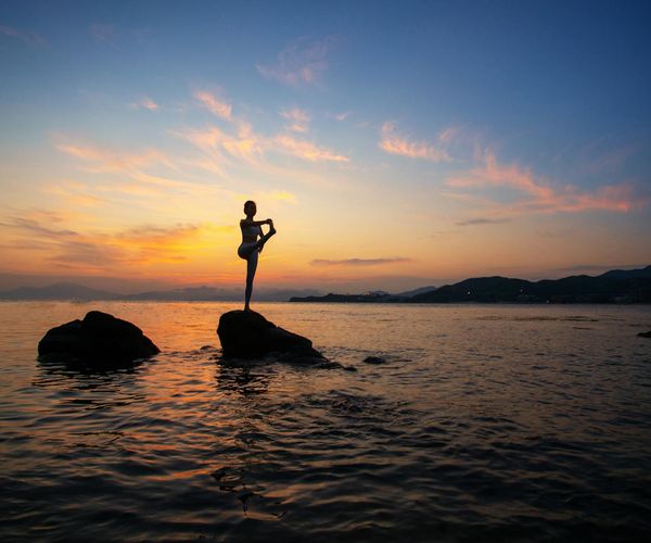 Silhouette of a person in a yoga pose against a sunrise.